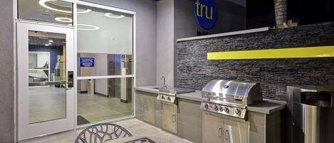 An outdoor kitchen area with a grill, a checkered table, and a glass door leading to an interior space.
