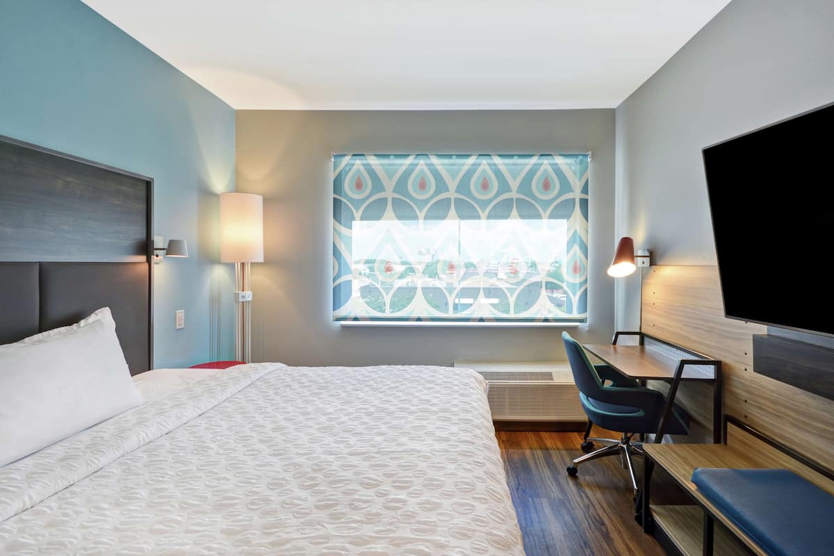 Une chambre d’hôtel équipée d’un lit, d’un bureau, d’une chaise et d’une grande télévision.
