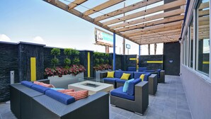 Un patio al aire libre con mobiliario de mimbre, una mesa de vidrio y plantas en macetas.