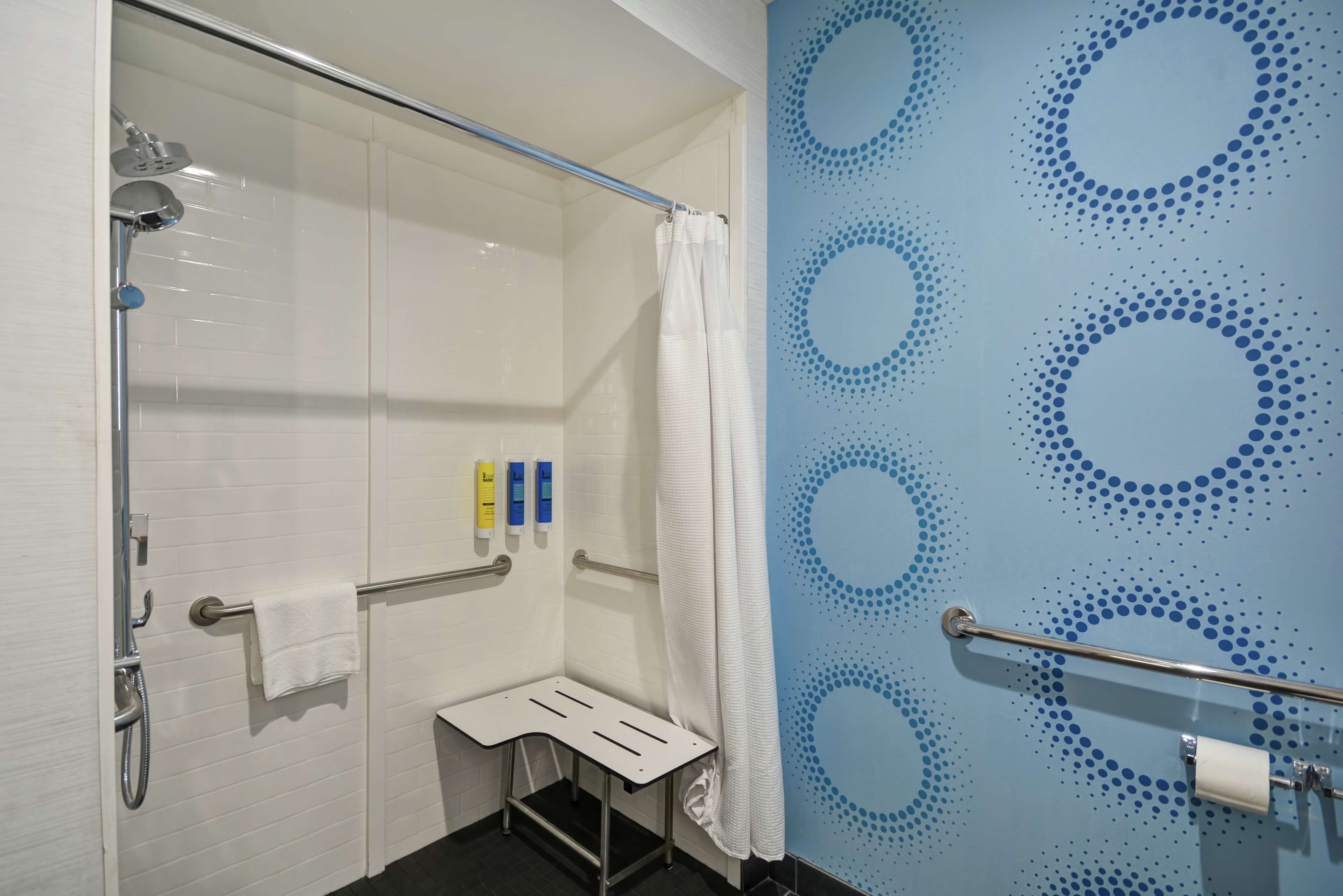 A bathroom with a glass shower enclosure, a white towel rack, a white towel, and a blue wall with circular patterns.