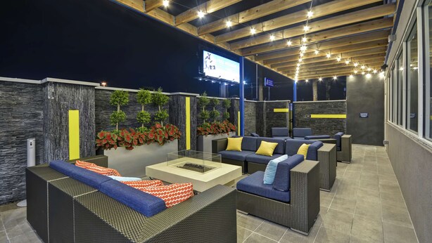 Un área de estar al aire libre con mobiliario de mimbre, una mesa de centro de vidrio y plantas decorativas.