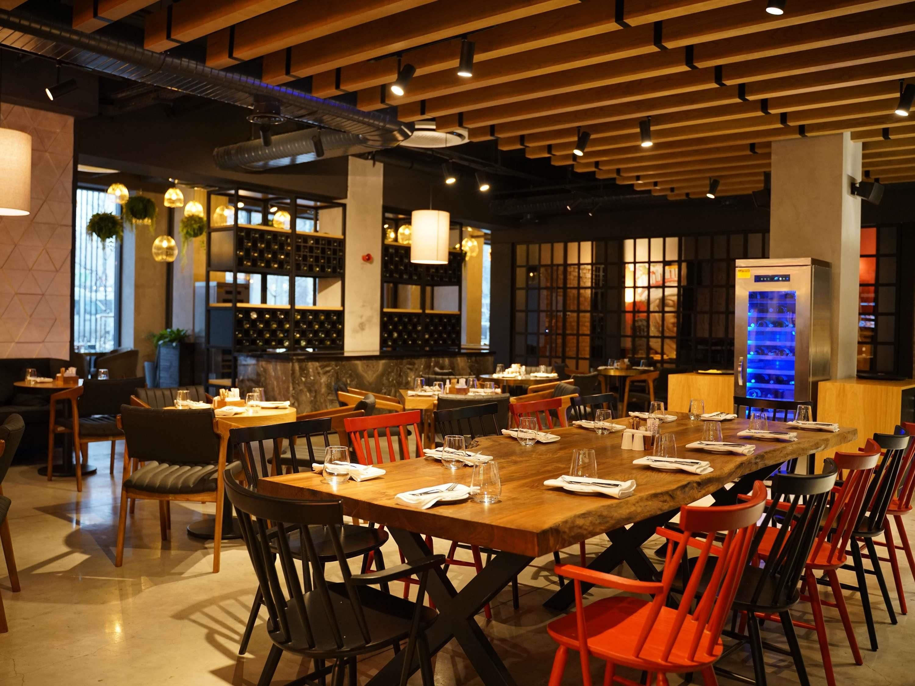 A restaurant with a long wooden table set for dining, surrounded by chairs.