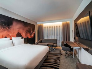 A hotel room with a bed, a desk, a chair, a large mirror, and a wall with a textured design.