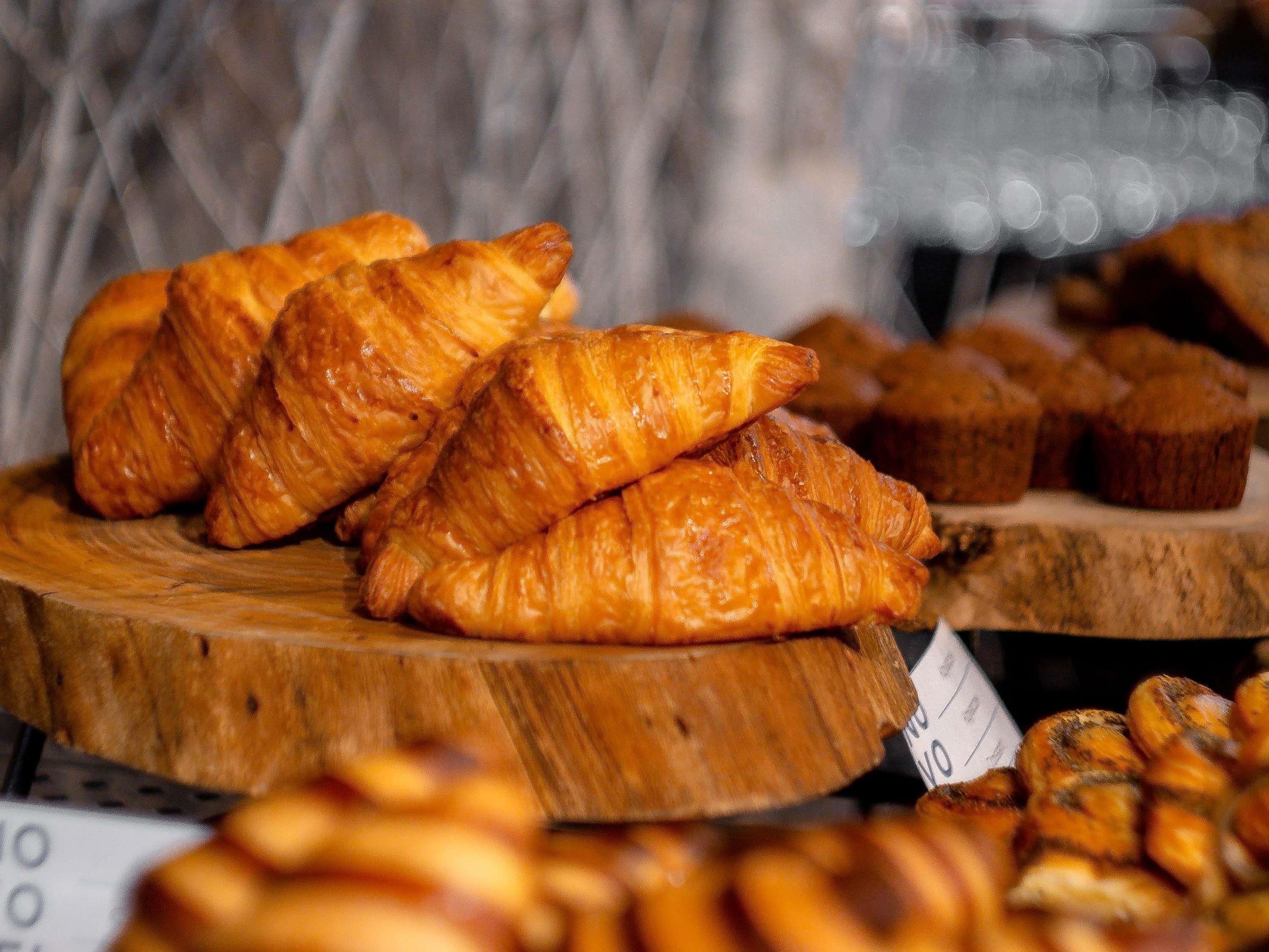 A display of pastries, including croissants and muffins, on wooden stands.