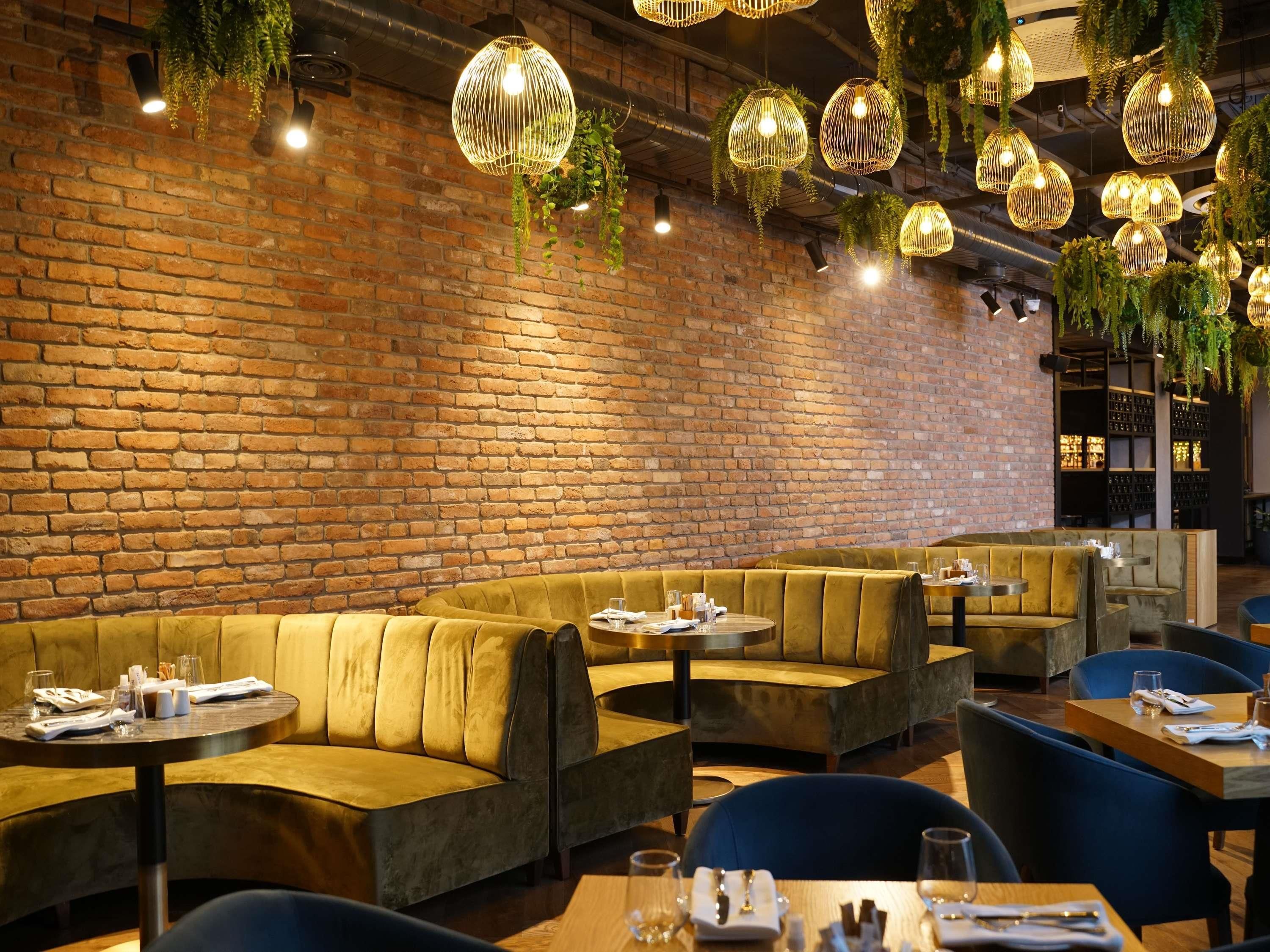 A restaurant with brick walls, hanging wicker lamps, and cushioned seating.