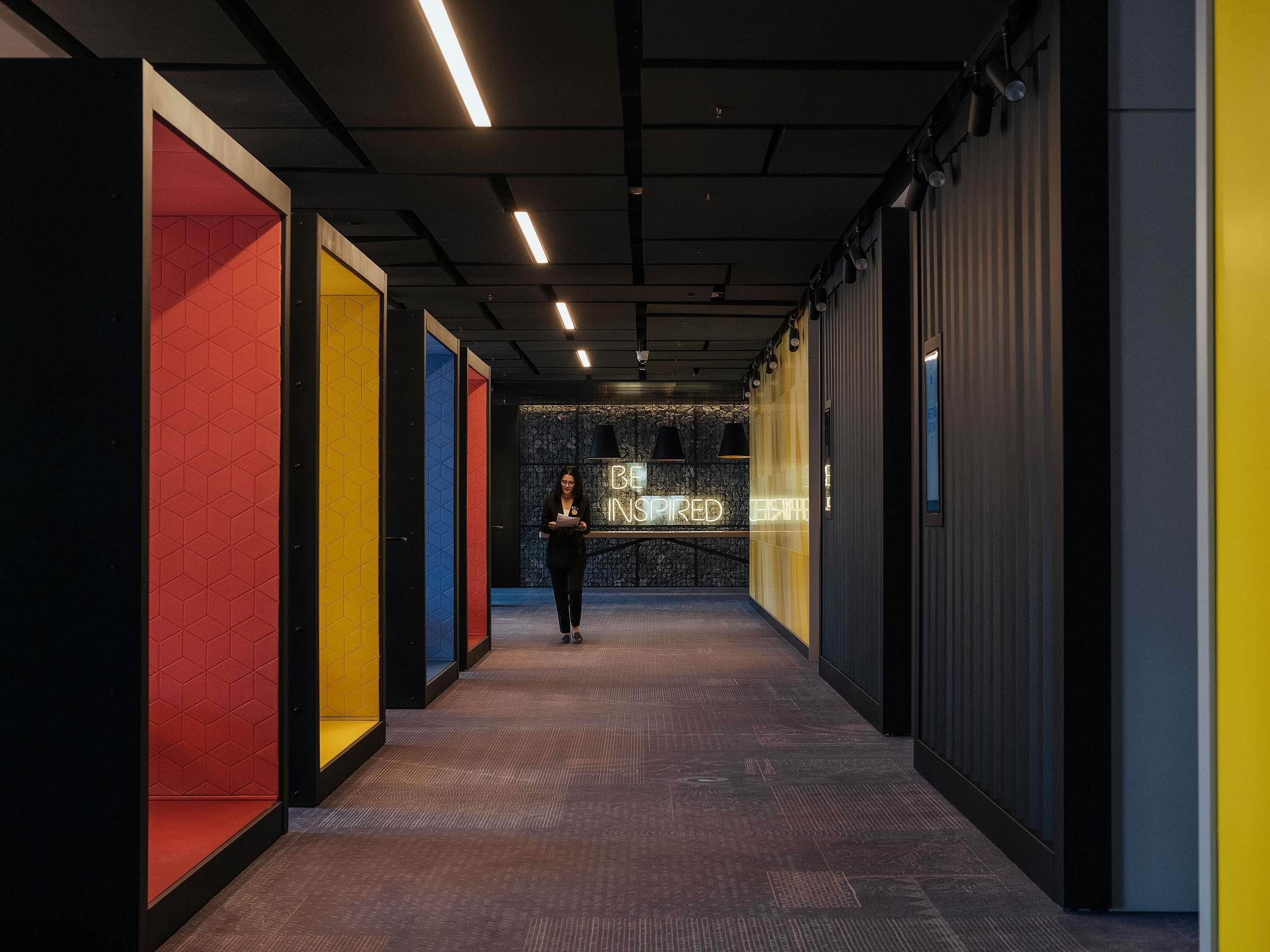 A corridor with a person walking, walls with geometric patterns, and a neon sign.