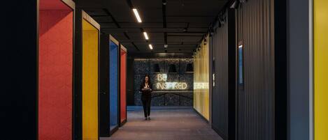 A corridor with a person walking, walls with geometric patterns, and a neon sign.