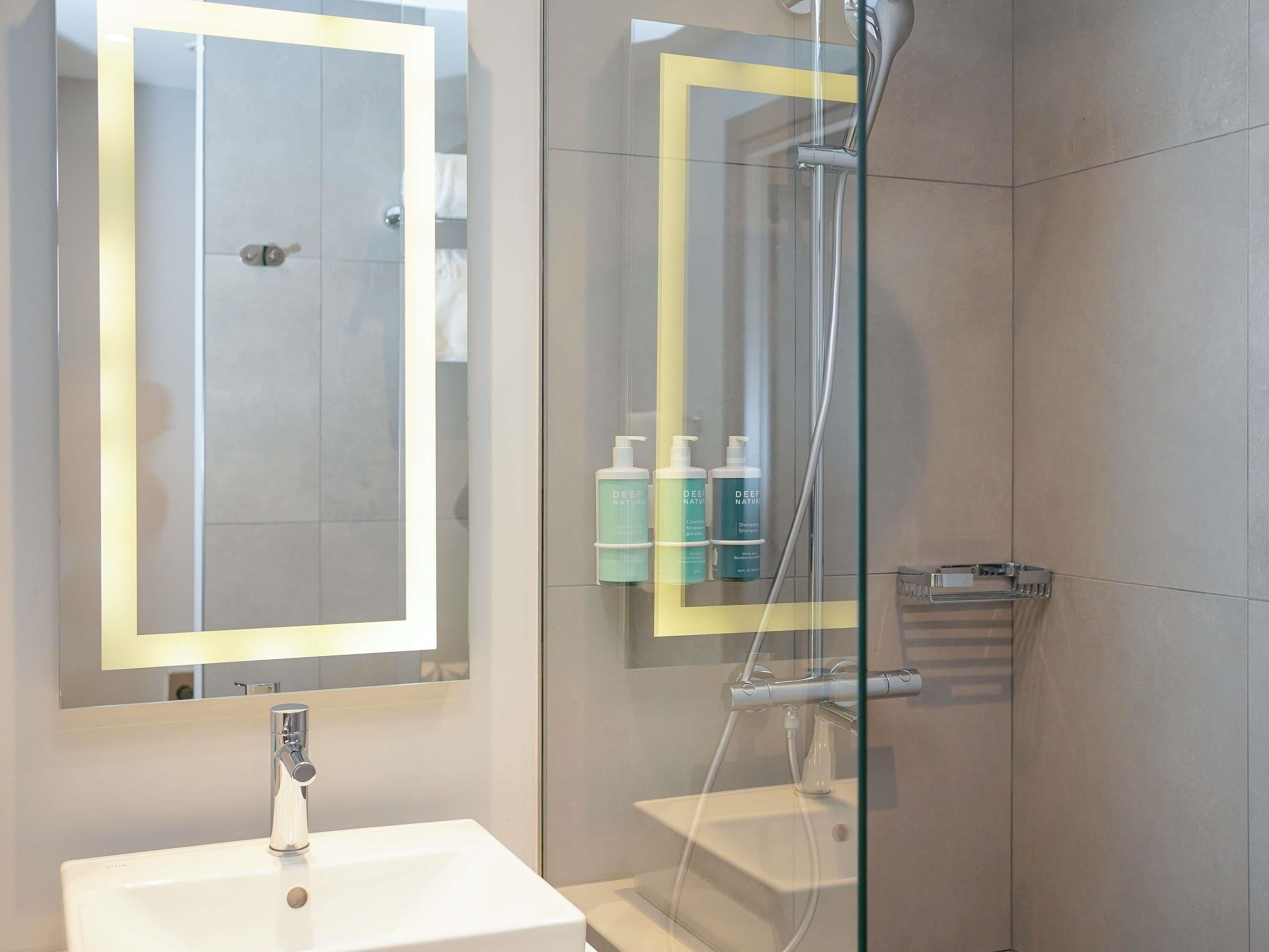 A bathroom with a glass-enclosed shower, a white sink, and a mirror with a lighted frame.