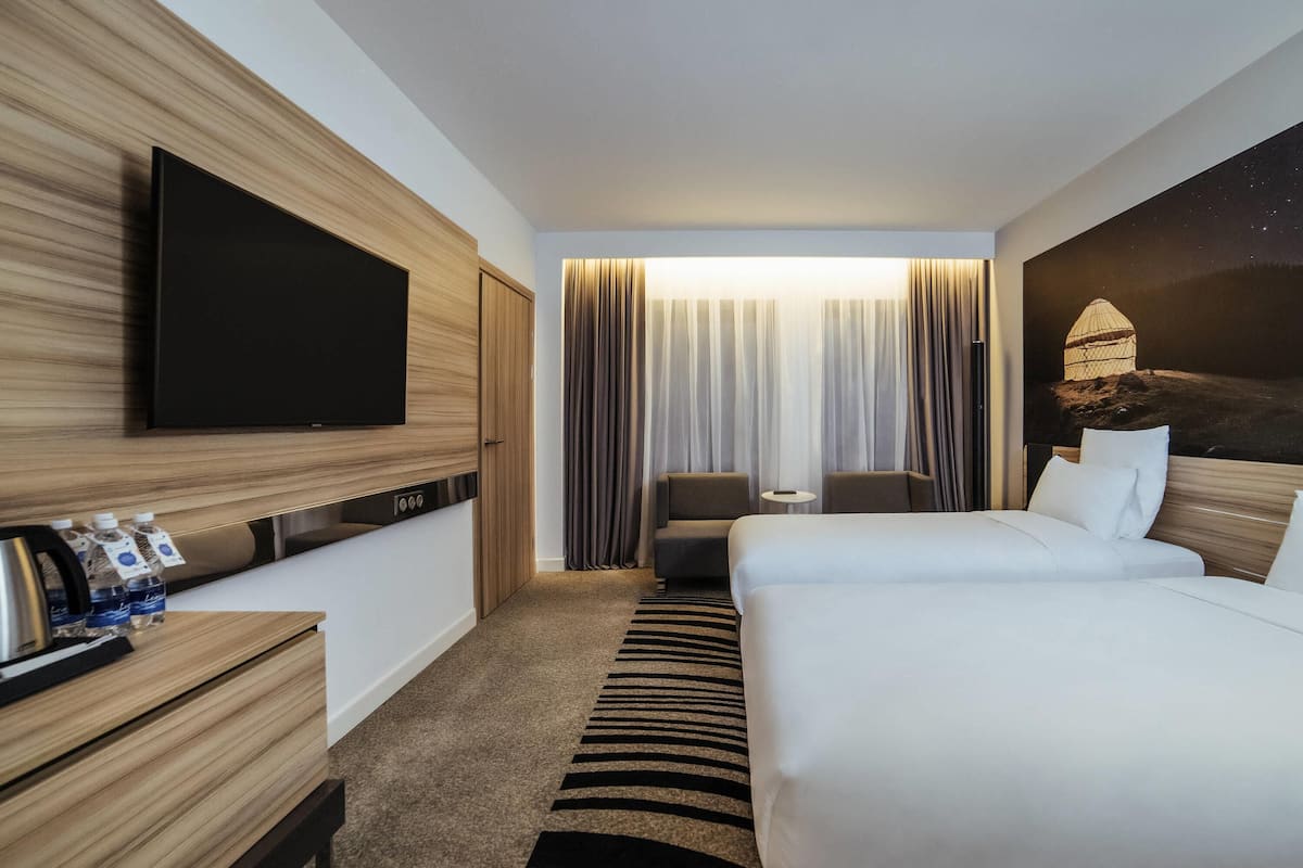 Une chambre d’hôtel équipée d’un lit, d’une télévision, d’un bureau avec une machine à café, d’une chaise et d’une fenêtre avec des rideaux.