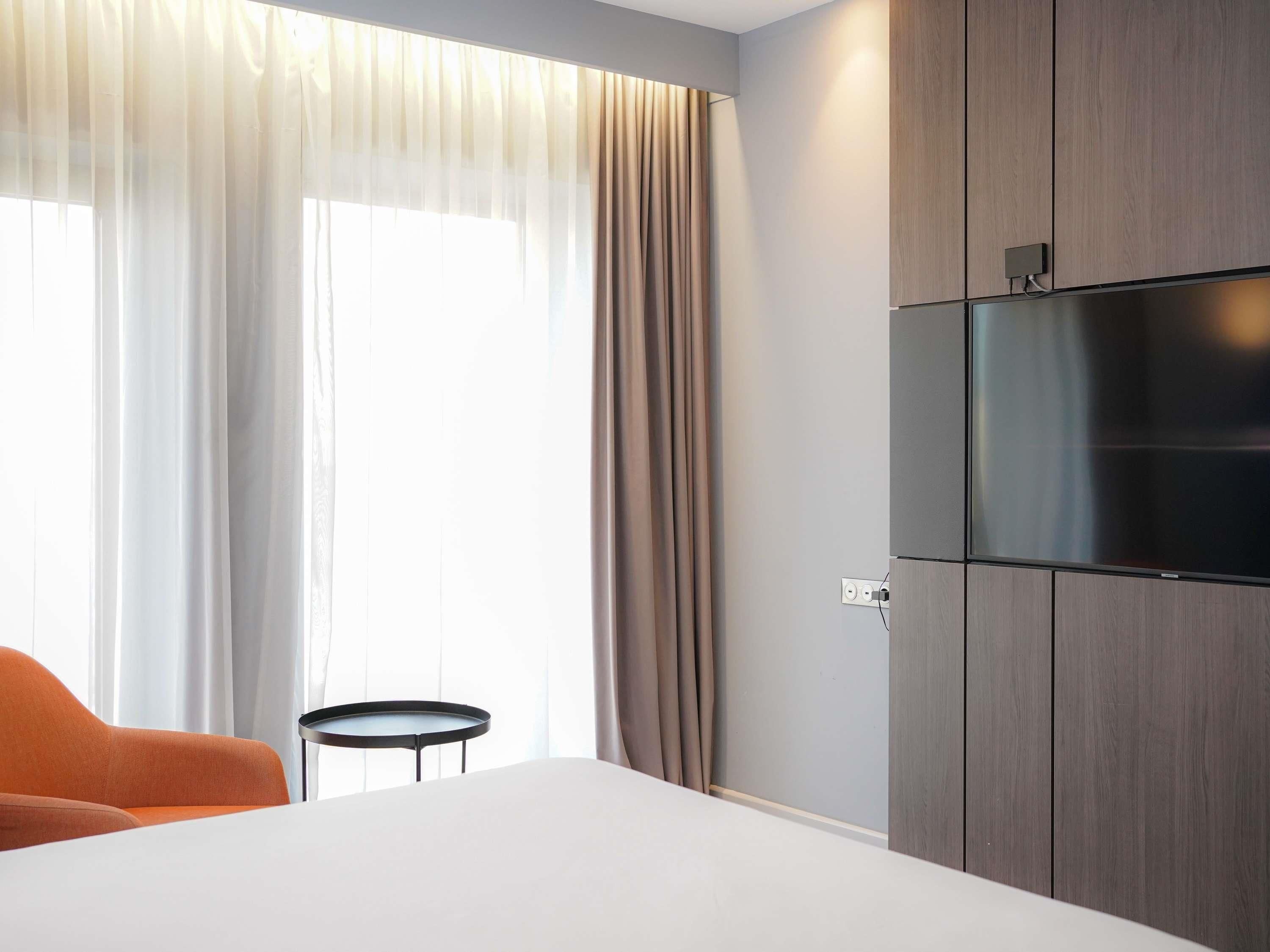 A hotel room with a bed, a TV mounted on the wall, a small round table, and a chair.