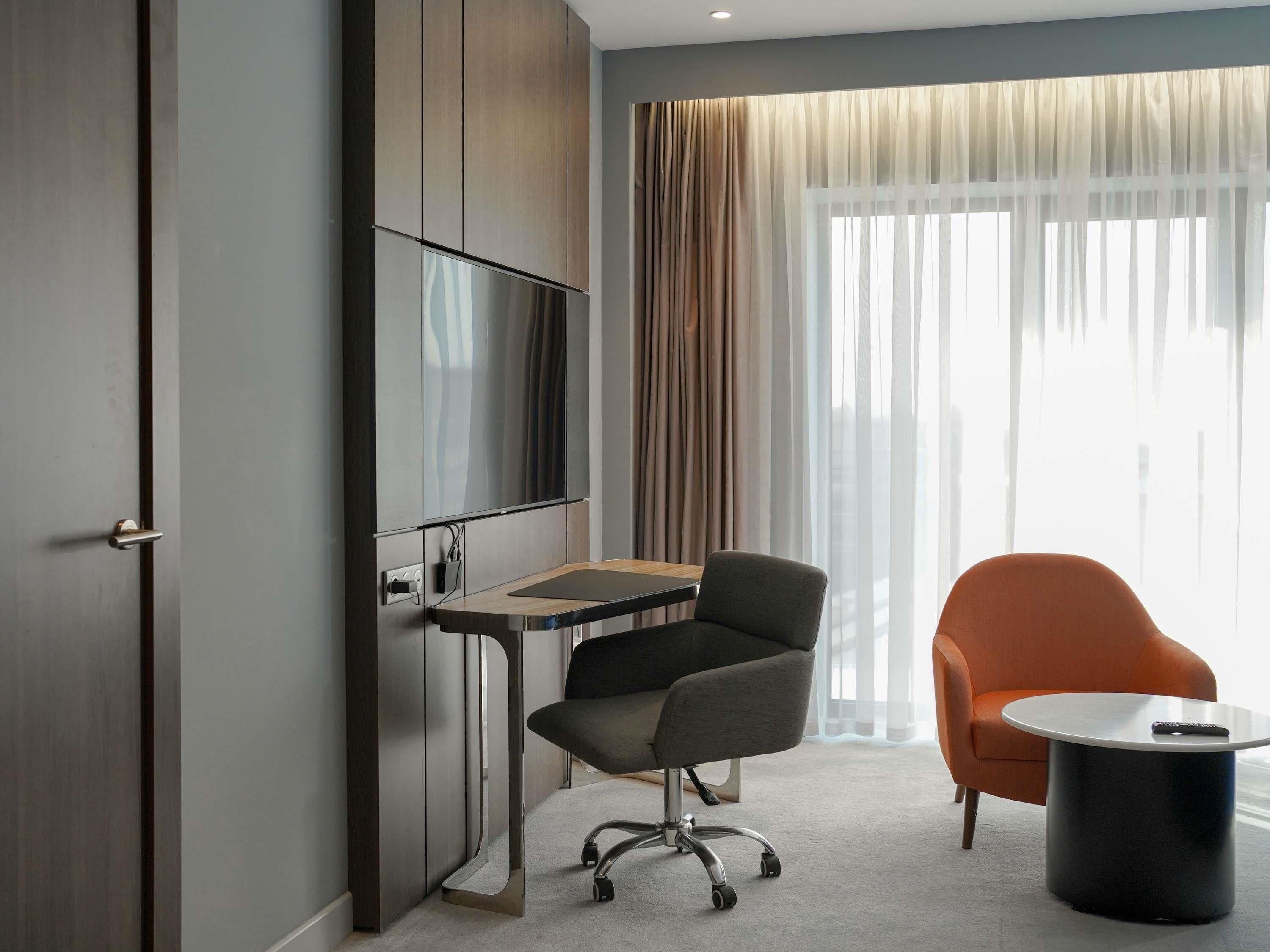 Habitación de hotel moderna con escritorio, silla de oficina y una mesa redonda.