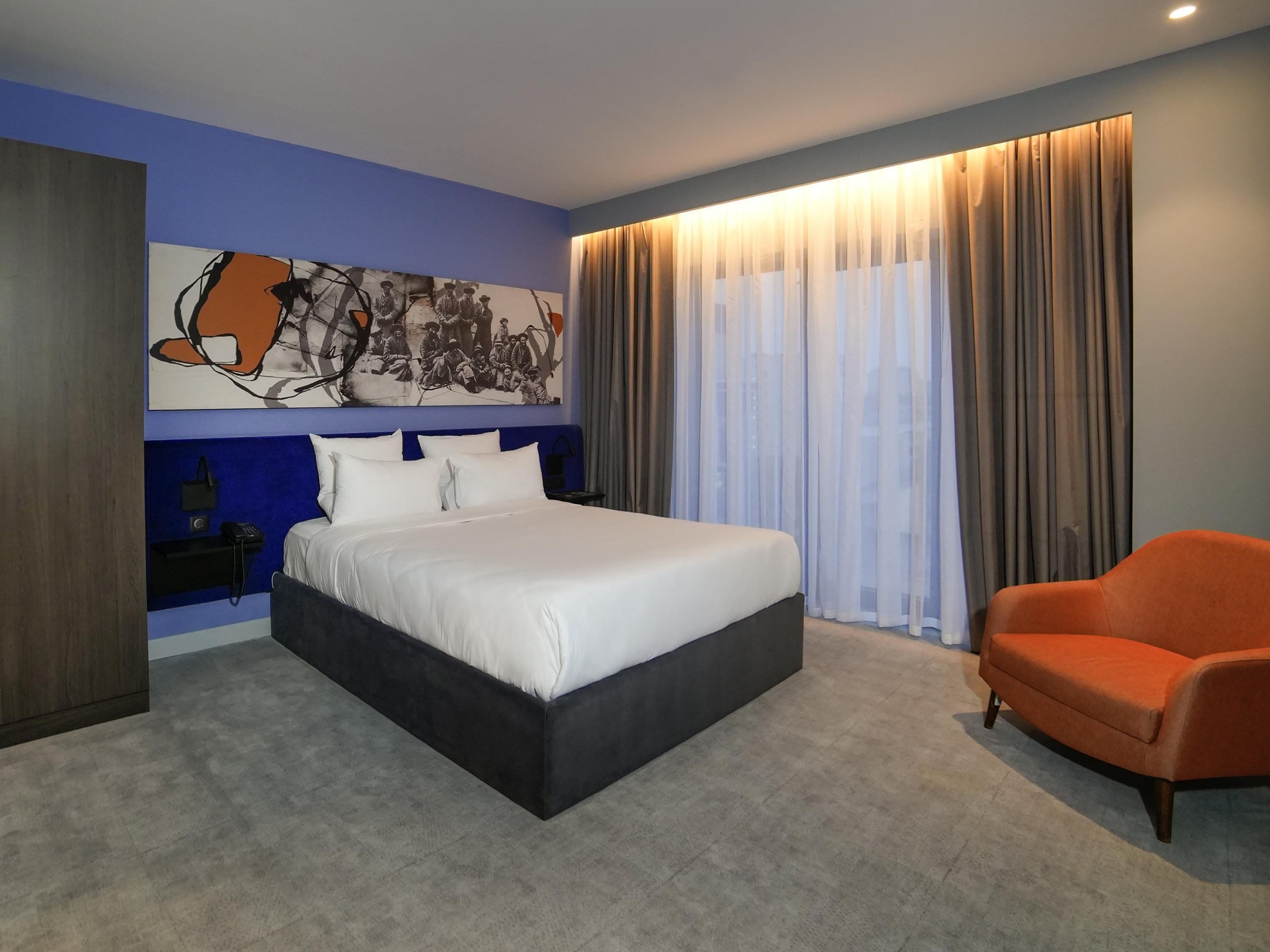 Una habitación de hotel moderna con una cama grande, una zona de estar y un cuadro en la pared.