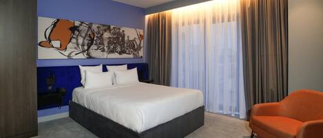 A modern hotel room with a large bed, a seating area, and a painting on the wall.