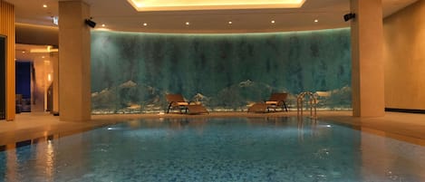 Piscina con sillones de descanso y una pared con cascada.
