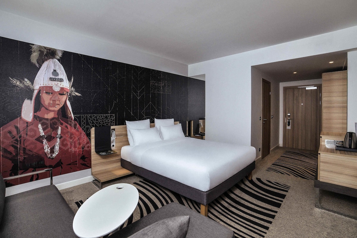 Une chambre d’hôtel moderne avec un grand lit, un canapé, une petite table et une fresque murale.
