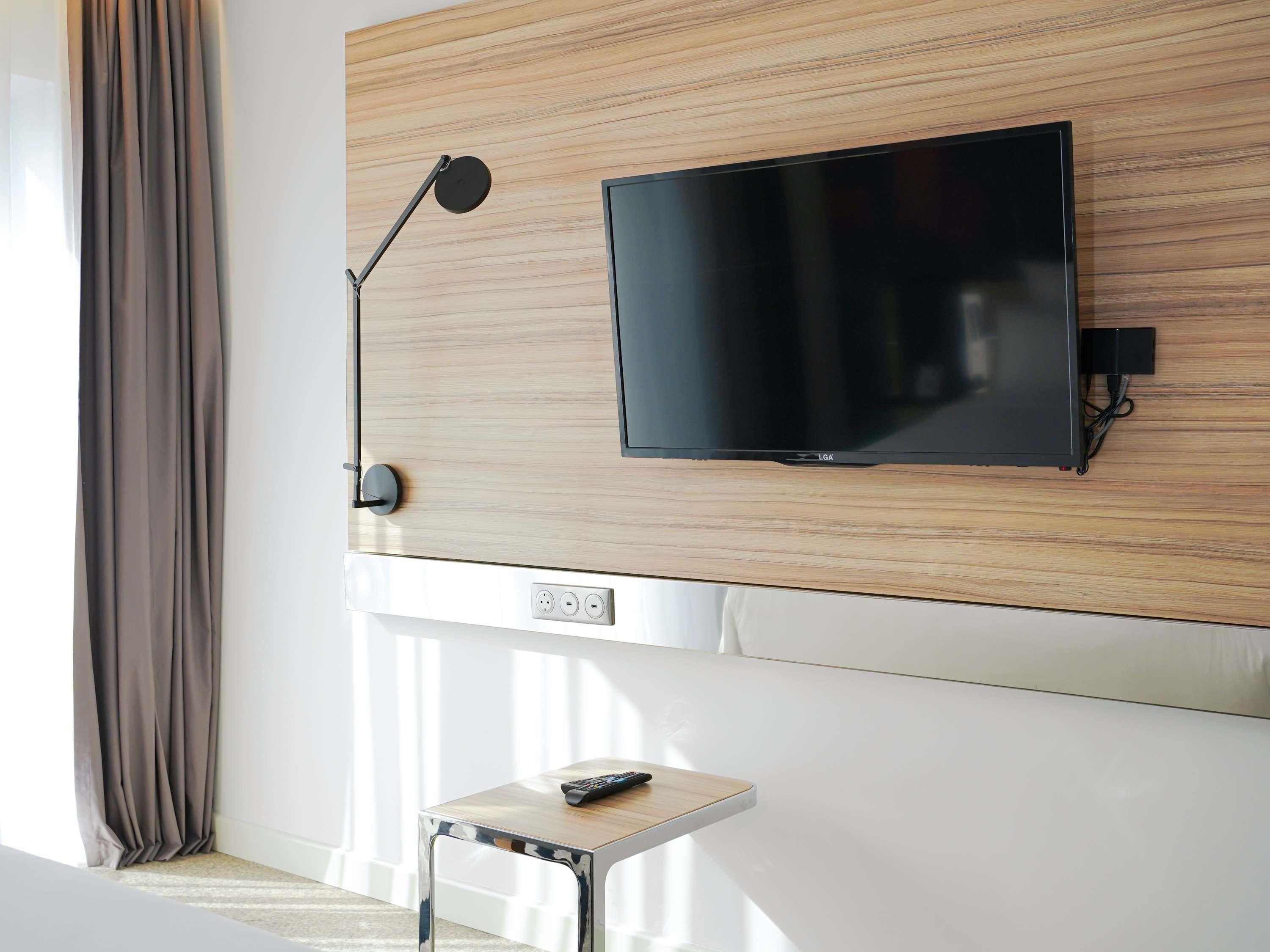 Ett modernt vardagsrum med en väggmonterad platt-TV, ett litet sidobord och en golvlampa.