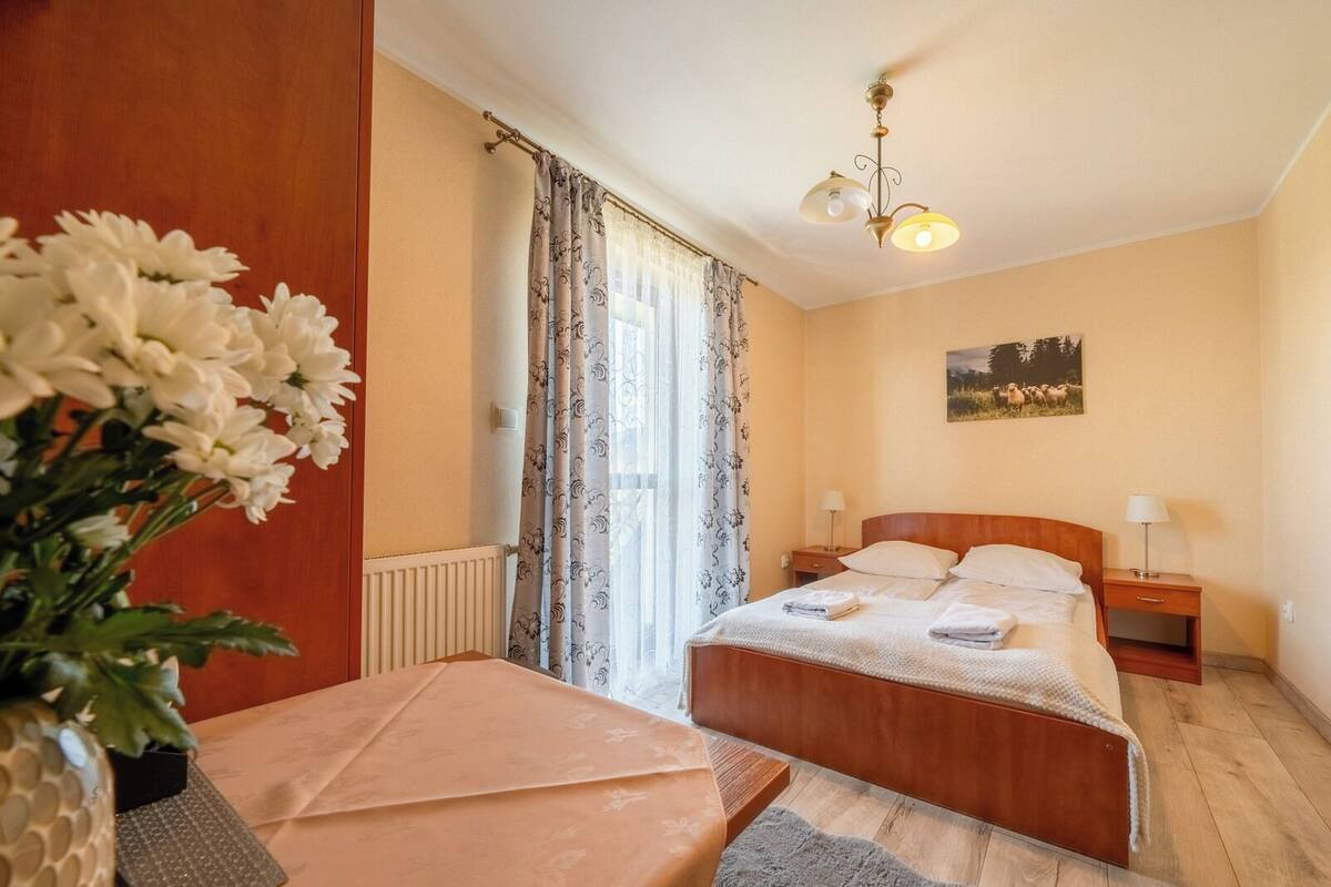 A hotel room with a wooden bed, a bedside table, a lamp, a radiator, and a window with curtains.