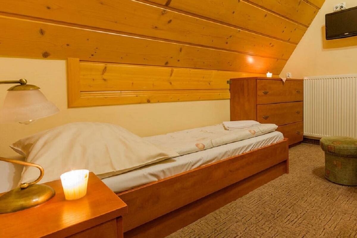 A single bed with a wooden headboard, a bedside table with a lamp, a dresser, and a radiator.