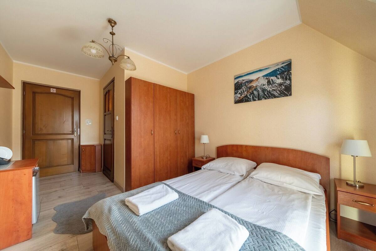 A hotel room with a bed, wooden wardrobe, and a painting on the wall.