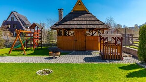 A wooden cabin with a thatched roof, a swing set, and a wooden playhouse in a grassy yard. - Willa u Anusia Jacuzzi & Sauna (Zakopane)