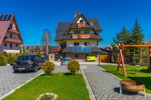 A two-story house with a sloped roof, a balcony, and a driveway leading to a parked car. - Willa u Anusia Jacuzzi & Sauna (Zakopane)