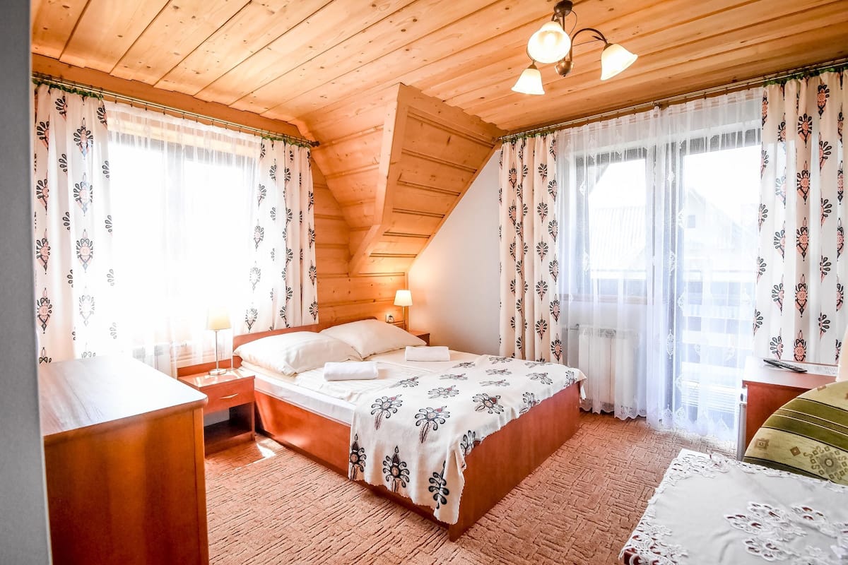 A wooden-paneled bedroom with a bed, nightstands, and a window with patterned curtains.