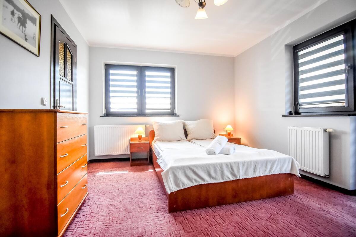 A bedroom with a wooden bed, a dresser, a radiator, and a window with blinds.