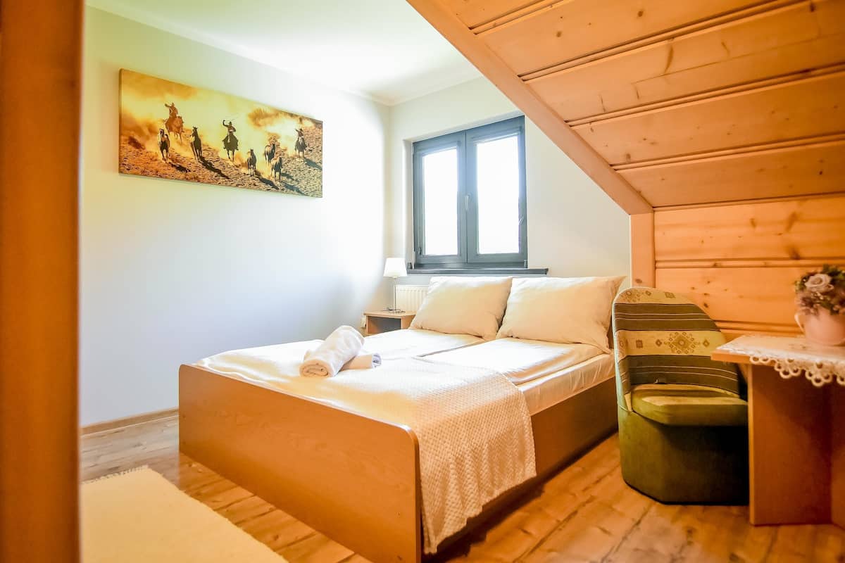 A bedroom with a bed, a nightstand, a window, and a painting on the wall.