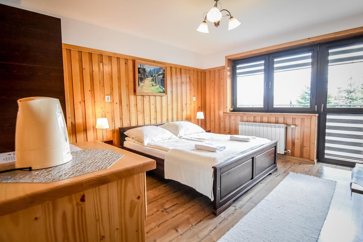 A wooden-paneled bedroom with a bed, bedside lamps, a painting, and a window with blinds.