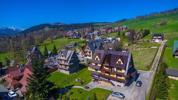 A traditional chalet-style building with a steeply pitched roof, a wooden deck, and a small garden area. - Willa u Zwijacza (Zakopane)