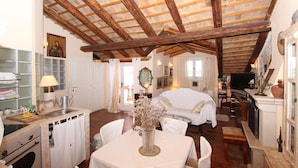 A rustic room with a wooden ceiling, a bed, a table with a vase, and a kitchen area. - Apartments Milkana (Rovinj)