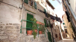 A narrow street with old buildings, potted plants on balconies, and clothes drying on lines. - Apartments Milkana (Rovinj)