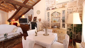 A cozy room with a white sofa, a dining table with chairs, a television, and a fireplace. - Apartments Milkana (Rovinj)