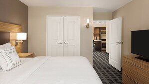 A hotel room with a bed, a TV, a wardrobe, and a door leading to a kitchenette. - TownePlace Suites by Marriott Cedar Rapids Marion (Marion)