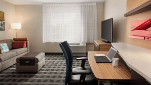 A hotel room with a sofa, a desk with a laptop, a TV, and a window with curtains. - TownePlace Suites by Marriott Cedar Rapids Marion (Marion)