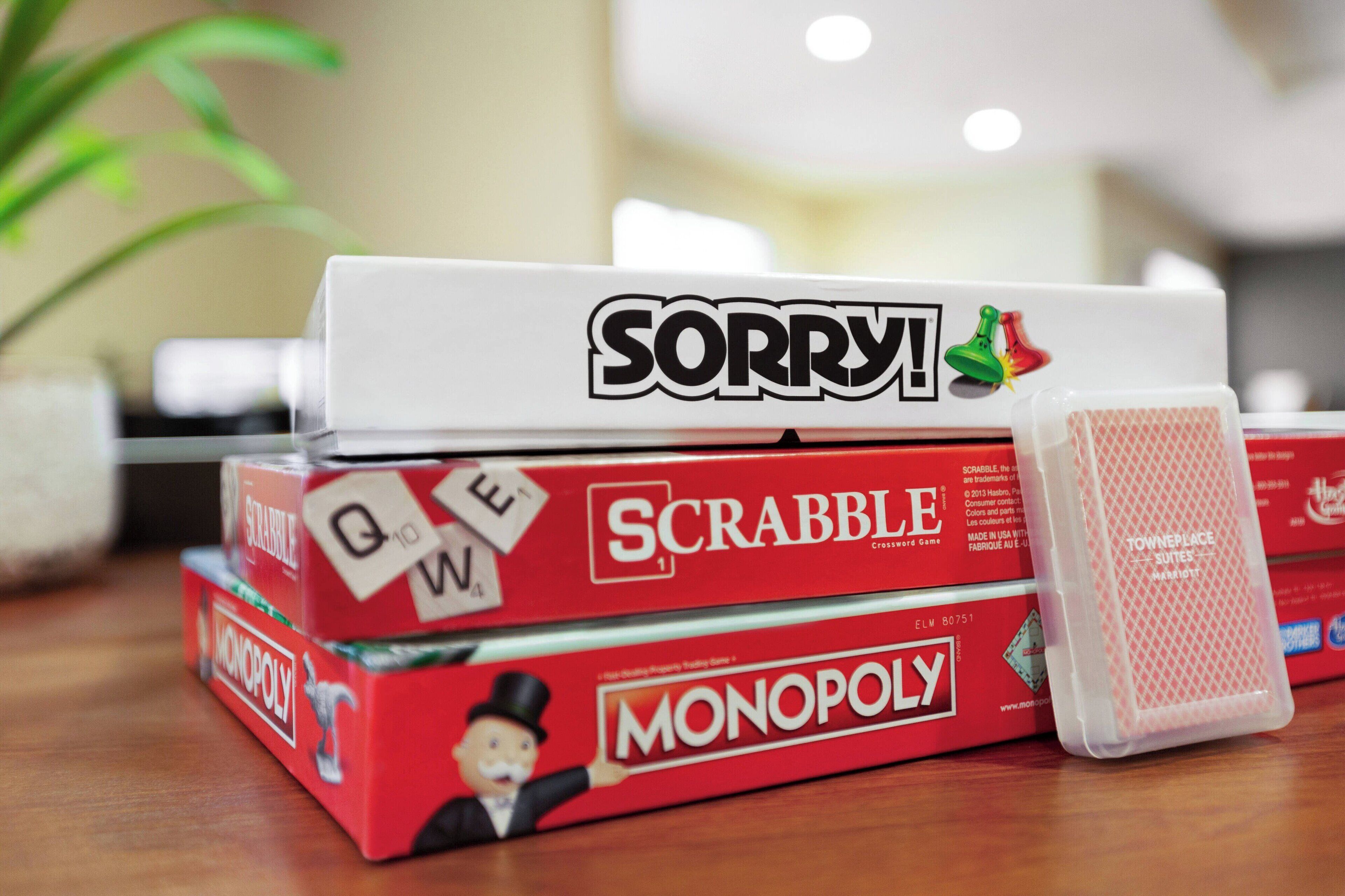Conjunto de jogos de tabuleiro, incluindo Scrabble, Monopoly e Sorry!, sobre uma superfície de madeira.