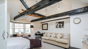 Une chambre à coucher moderne avec un lit, un canapé, un bureau et une chaise. On y trouve une fenêtre avec des rideaux, une horloge au mur et un tableau encadré.