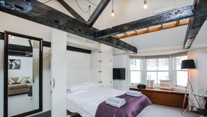Quarto com cama, espelho grande, televisão e janela com cortinas.