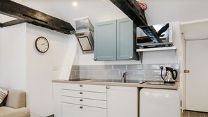 Uma cozinha compacta com armários brancos, forno embutido e máquina de café no balcão.