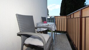 A wicker chair and a table with a plaid tablecloth, positioned against a wall with a metal fence. - Apartments Miriana (Rovinj)