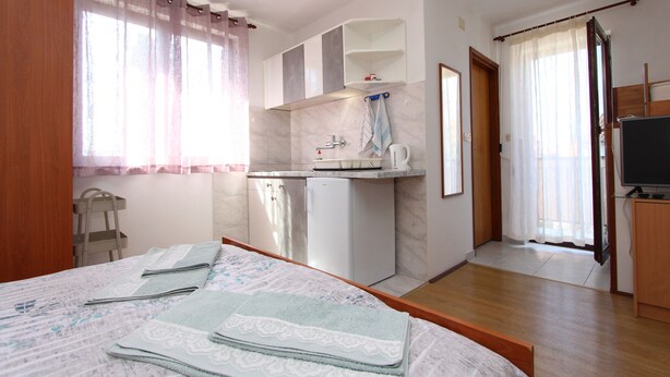 A bedroom with a bed, a small kitchenette, a television, and a bathroom visible through an open door. - Apartments Miriana (Rovinj)