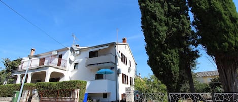 A two-story white building with balconies, a blue umbrella, and a stone wall in front.