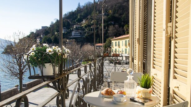 A terrace with a table set for a meal, overlooking a body of water and a hillside.