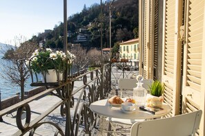 A terrace with a table set for a meal, overlooking a body of water and a hillside. - Casa Stoppani - WelcHome (Cannobio)