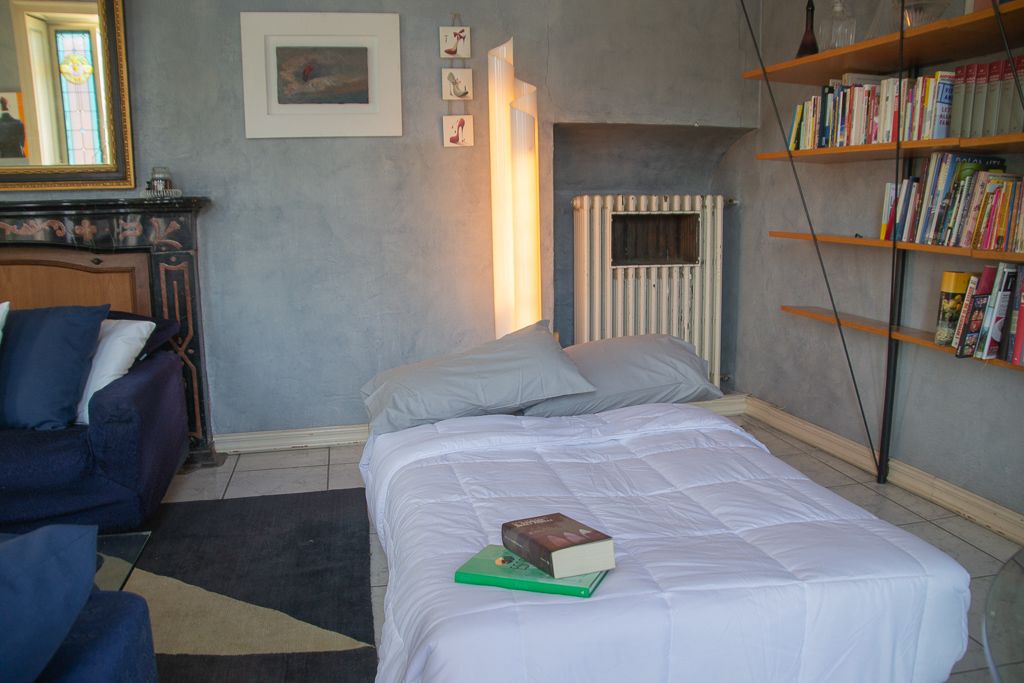 A bedroom with a bed, a chair, a bookshelf, a radiator, and a mirror.