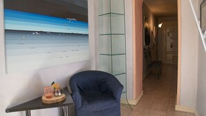 A hallway with a glass partition, a blue chair, and a framed artwork on the wall.