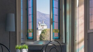 A dining area with a glass table and red chairs, a window with stained glass, and a view of a building.