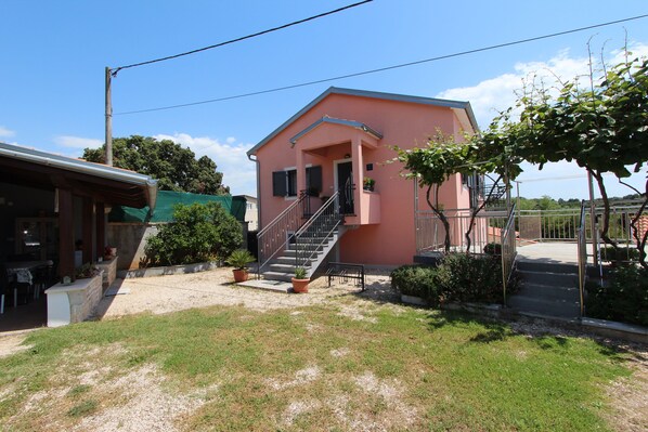 A pink building with a staircase leading to the entrance, surrounded by greenery and a clear sky.