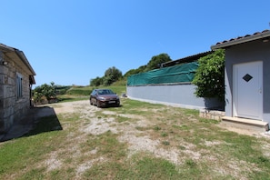A stone building with a car parked in front, a small shed, and a grassy area.