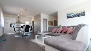 A modern living room with a grey sofa, a glass coffee table, and a kitchen in the background. - Apartment Mondelaco (Rovinj)